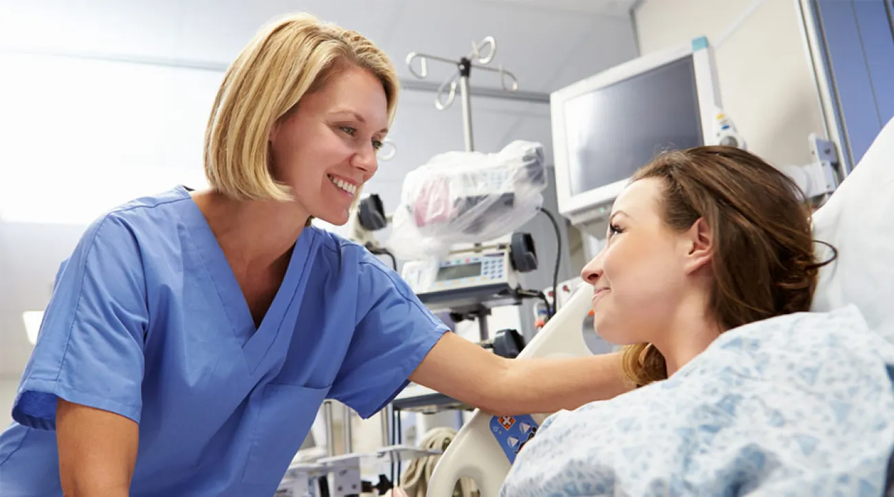 Female nurse helps female patient get situated in hospital room