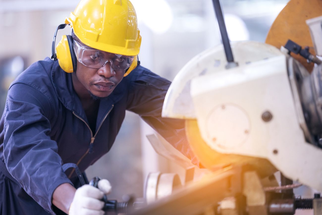 Black man in yellow hardhat and jumpsuit focuses on keeping machine steady. Example of the importance of reskilling