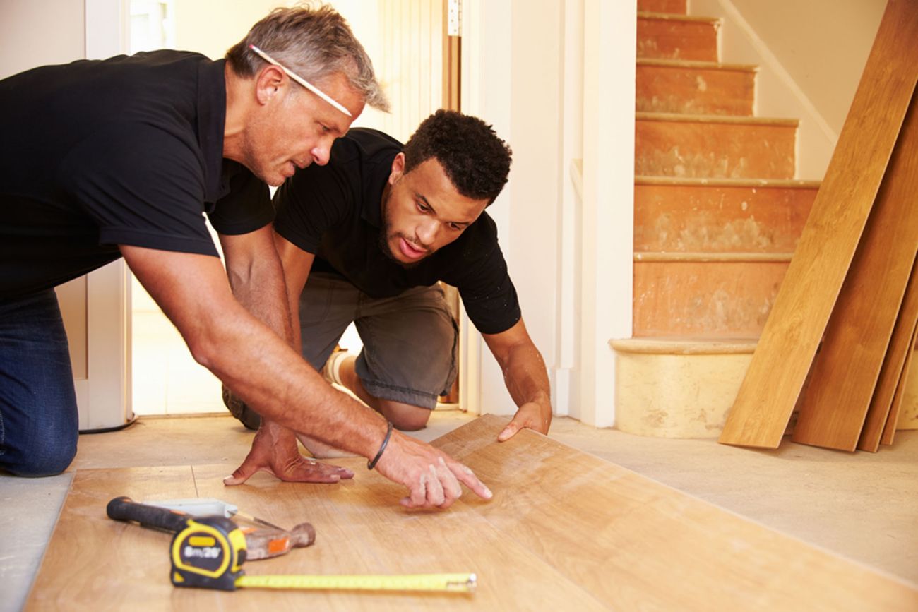 White older male works with younger black male on a floor. Example of on-the-job training and apprenticeships