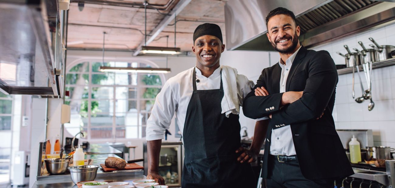 Black male kitchen manager smiles with the restaurant manager in the kitchen