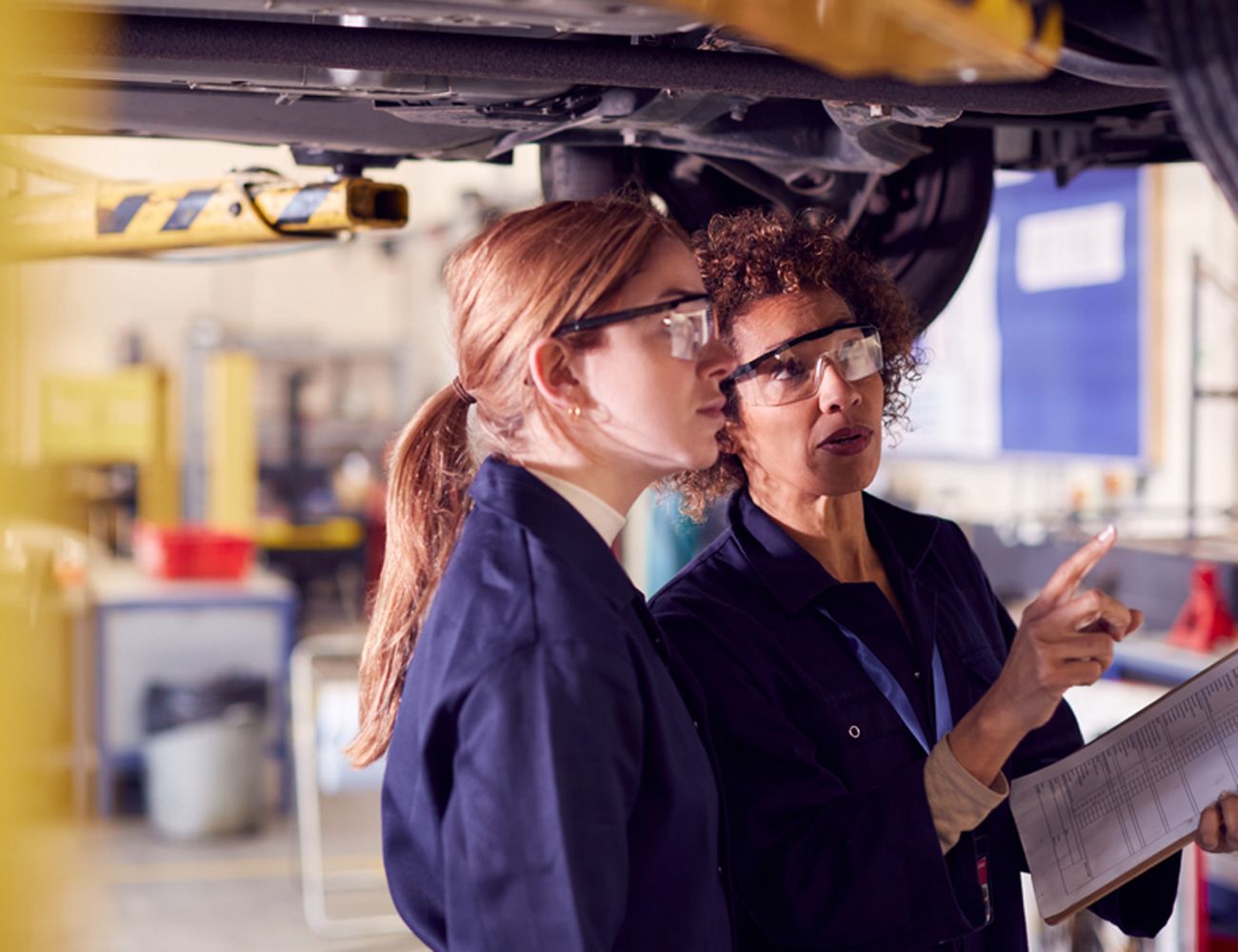 Female instructor shows a student different mechanisms on the underside of a car