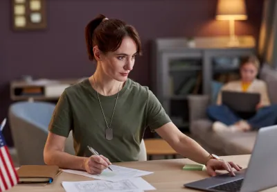 Young military woman uses a laptop as her daughter works in the background