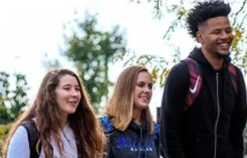 Three students walk together through campus on a bright autumn day.