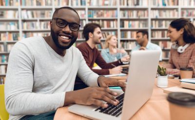 Young Black man works on a laptop in the library, doing financial aid research