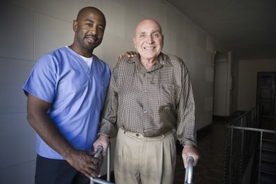 male certified nursing assistant helps patient get around with a walker