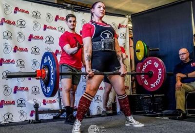 Weightlifter Angeline Deluca stands holding a straight bar with weights on either end