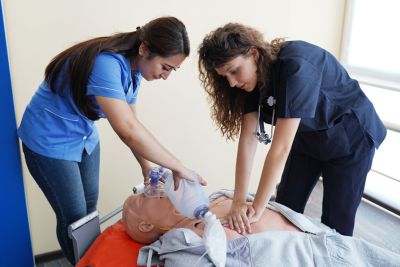Two nursing students learn how to save real patients by practicing CPR on a dummy in a healthcare setting