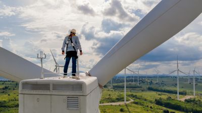 Wind turbine technician stands on the nacelle at the top of a wind turbine