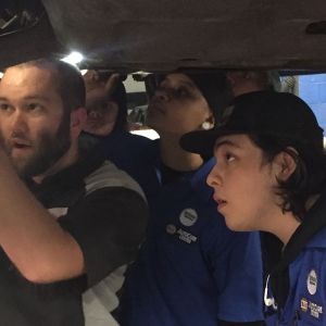 Auto mechanic Jake Sorenson shows two technicians how to fix something on a car