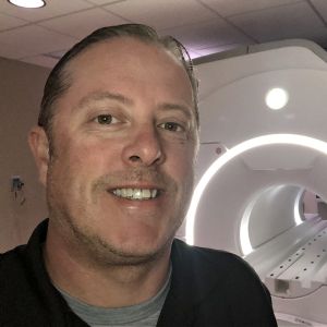 Joe Seibert, MRI technician, stands in front of an MRI machine