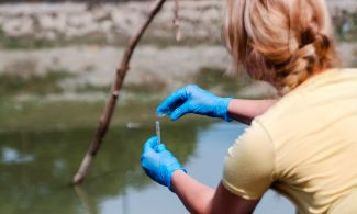 An environmental field technician collects a water sample 